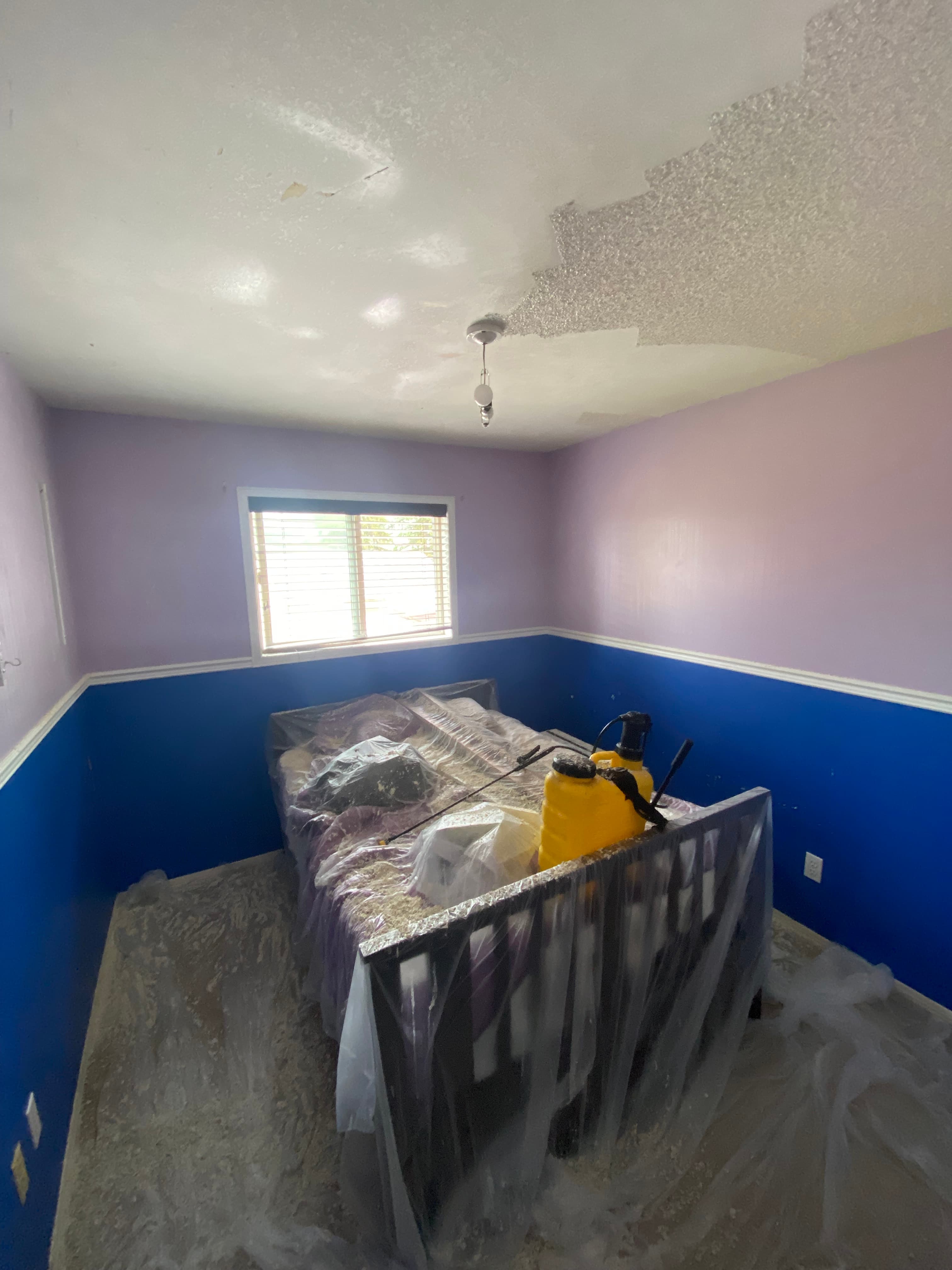 Popcorn ceiling texture removal in progress with plastic protection on windows and furniture
