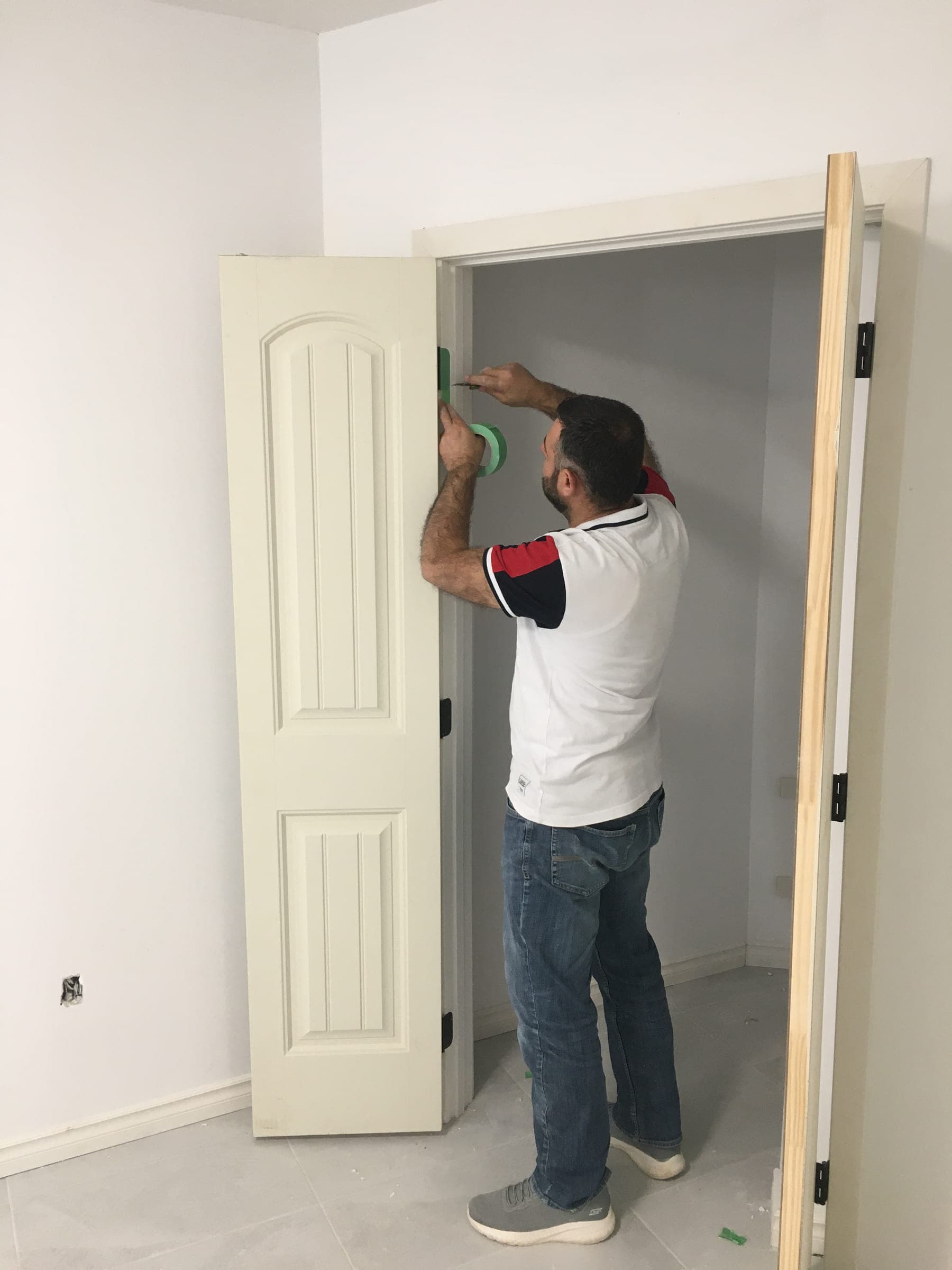 Painter masking a door frame with tape before painting the trim