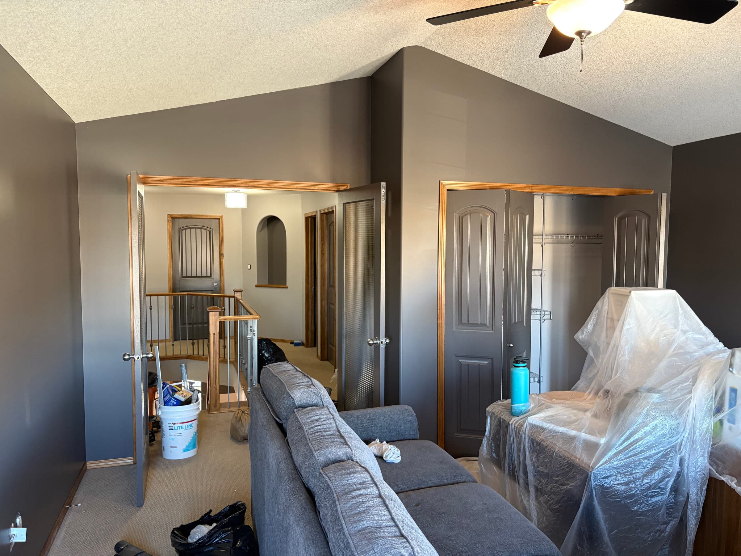 Upstairs room repainted in charcoal grey, with furniture wrapped in plastic and the paint pail still out